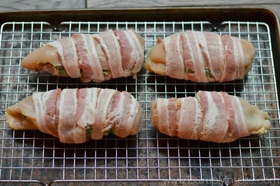 four uncooked chicken breasts wrapped in bacon on a baking sheet
