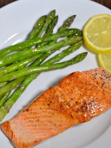 Pan Seared Salmon on a white plate with asparagus and lemon slices