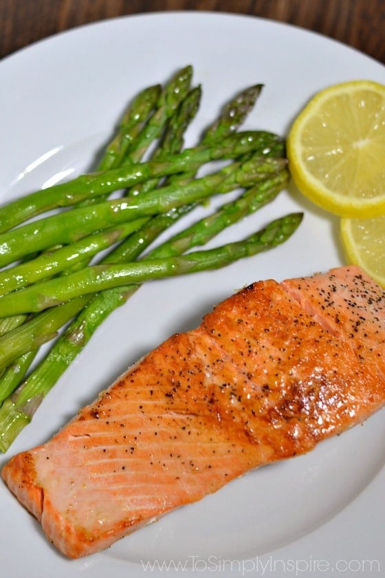 Pan Seared Salmon on a white plate with asparagus and lemon slices