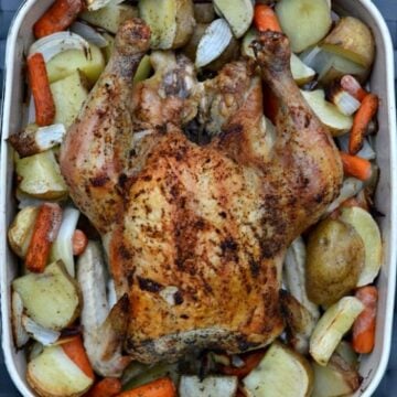 a casserole dish with a whole chicken surrounded by cut potatoes, and carrots