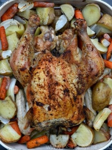 closeup of a dish with a whole chicken surrounded by cut potatoes, and carrots