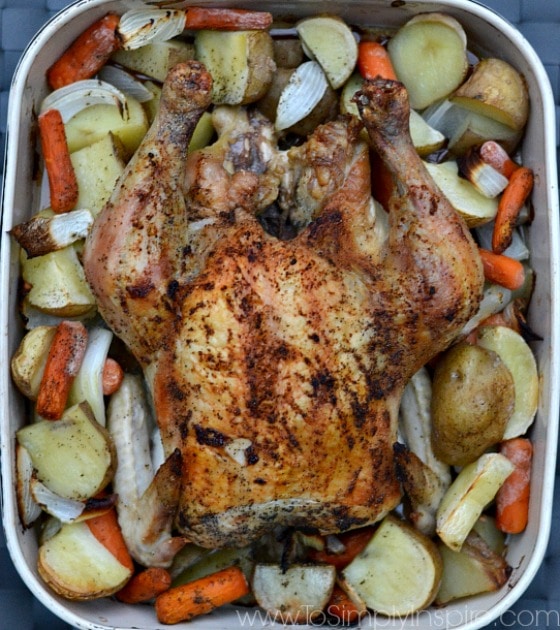 a casserole dish with a whole chicken surrounded by cut potatoes, and carrots