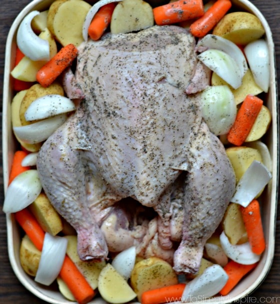 a uncooked whole chicken in a baking dish with potatoes onions and baby carrots