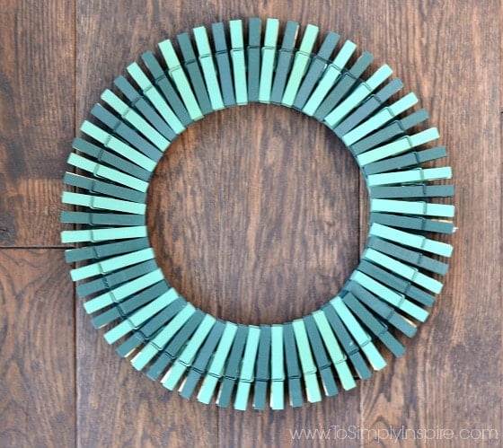 a wreath made out of painted green clothespins on a wood table