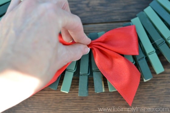 woman placing a red bow on a clothespin wreath