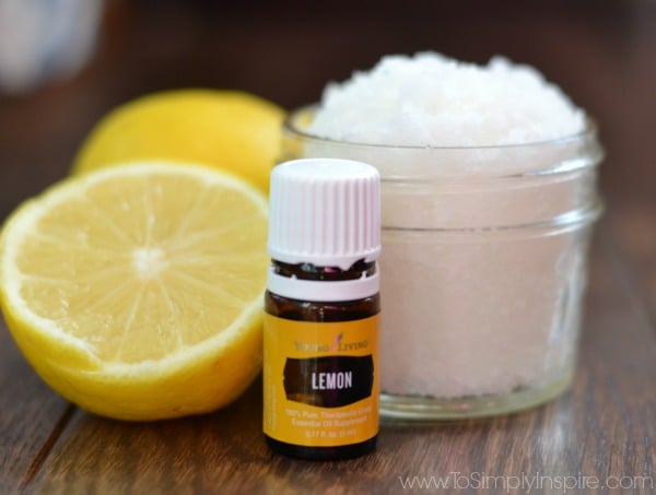 a small mason jar with lemon sugar scrub and a half a lemon and a bottle of lemon essential oil beside