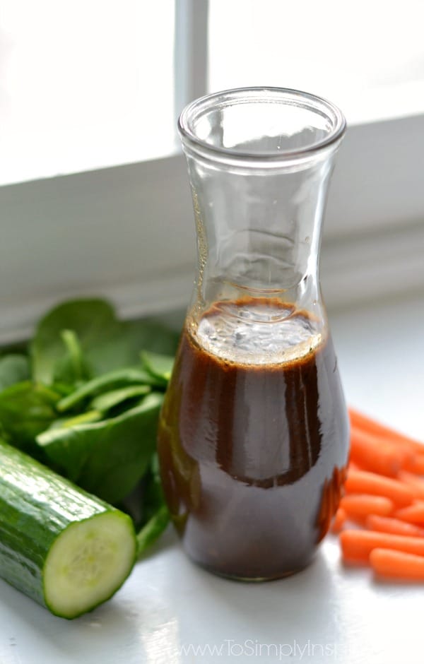a bottle of homemade balsamic vinaigrette surrounded by fresh carrots and cucumber 
