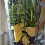 A blender filled with spinach oranges and blueberries