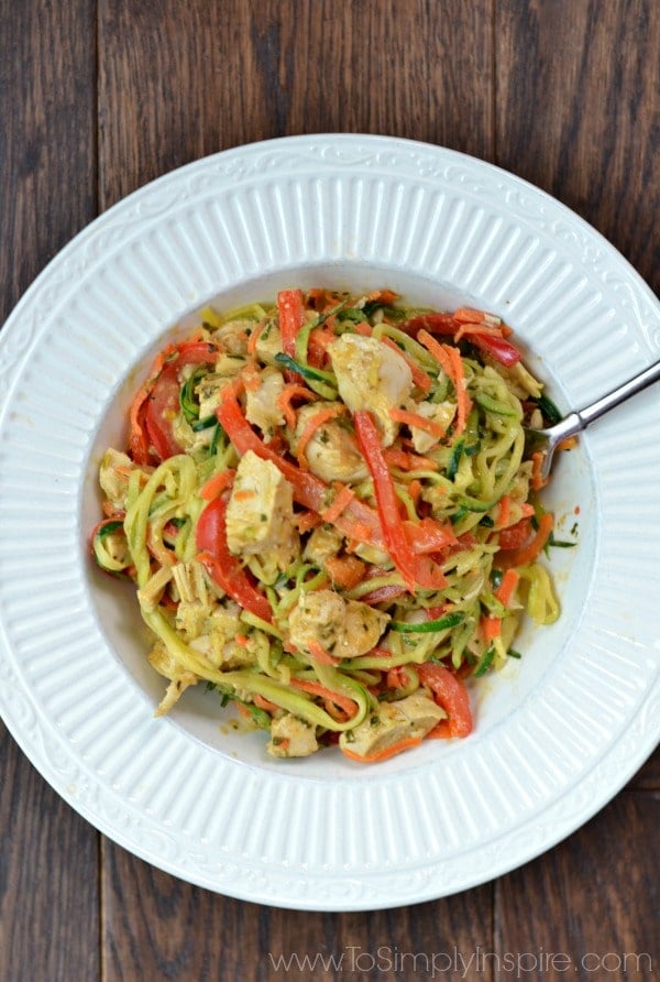 A closeup of a white bowl zucchini noodles, chicken and sliced red peppers