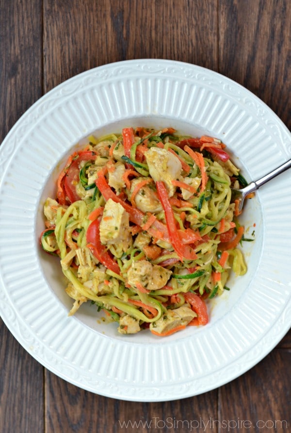 A closeup of a white bowl zucchini noodles, chicken and sliced red peppers