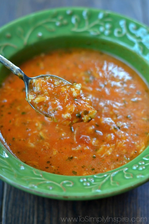 A spoonful of chicken tomato basil soup over a green bowl 