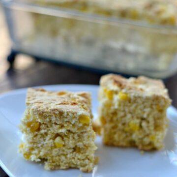 two pieces of cornbread on a white plate with a glass dish in the background