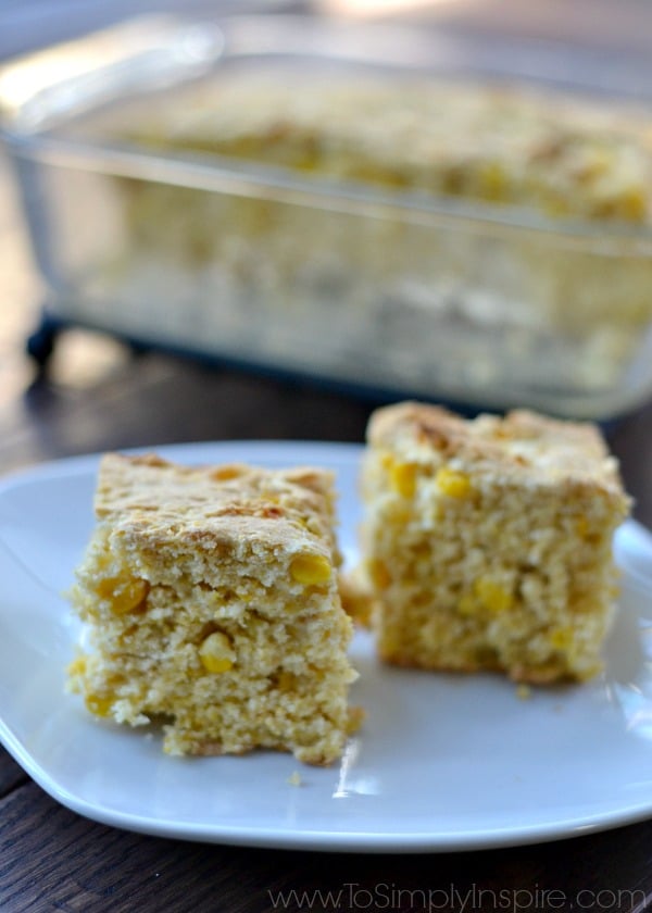 two pieces of cornbread on a white plate with a glass dish in the background