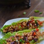 A plate of two lettuce wraps with ground turkey meat and red peppers