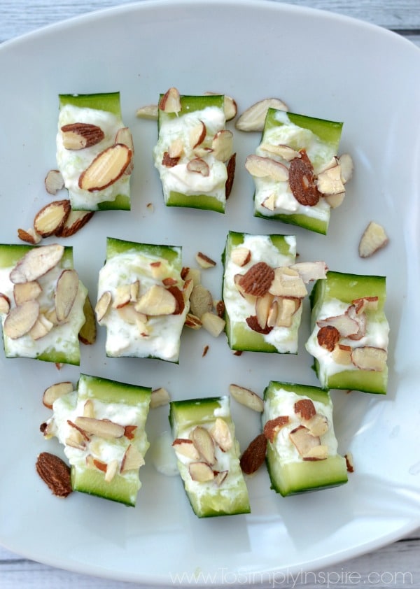A bunch Cucumber slices topped with almonds and Feta on a white plate
