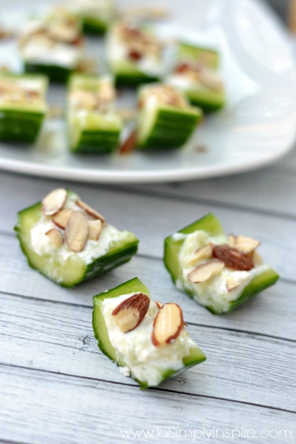 three cucumber slices with feta and almond slices with a plate full in the back