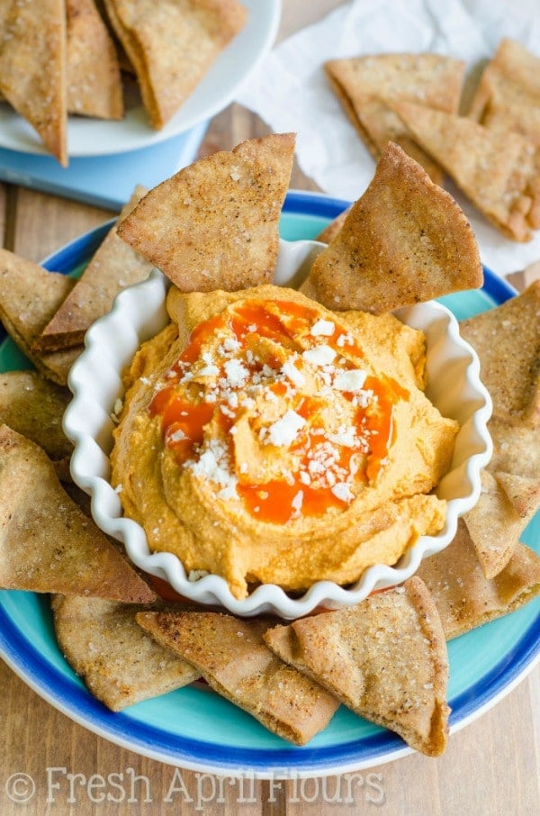 A white bowl with buffalo hummus with crackers