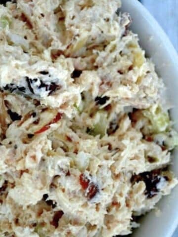 a white bowl full of chicken salad with cranberries