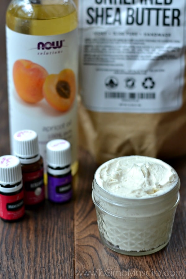 a mason jar with lotion on a table with 3 essential oil bottles and apricot oil in the background