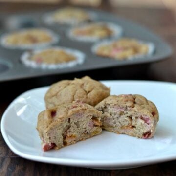 a plate with two banana rhubarb muffins with a muffin tin in the background
