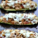 three chicken stuffed zucchini boats on a baking sheet