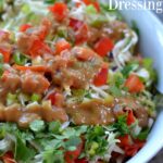 A close up of a bowl of lettuce with diced red peppers and a Thai peanut butter dressing drizzled on top