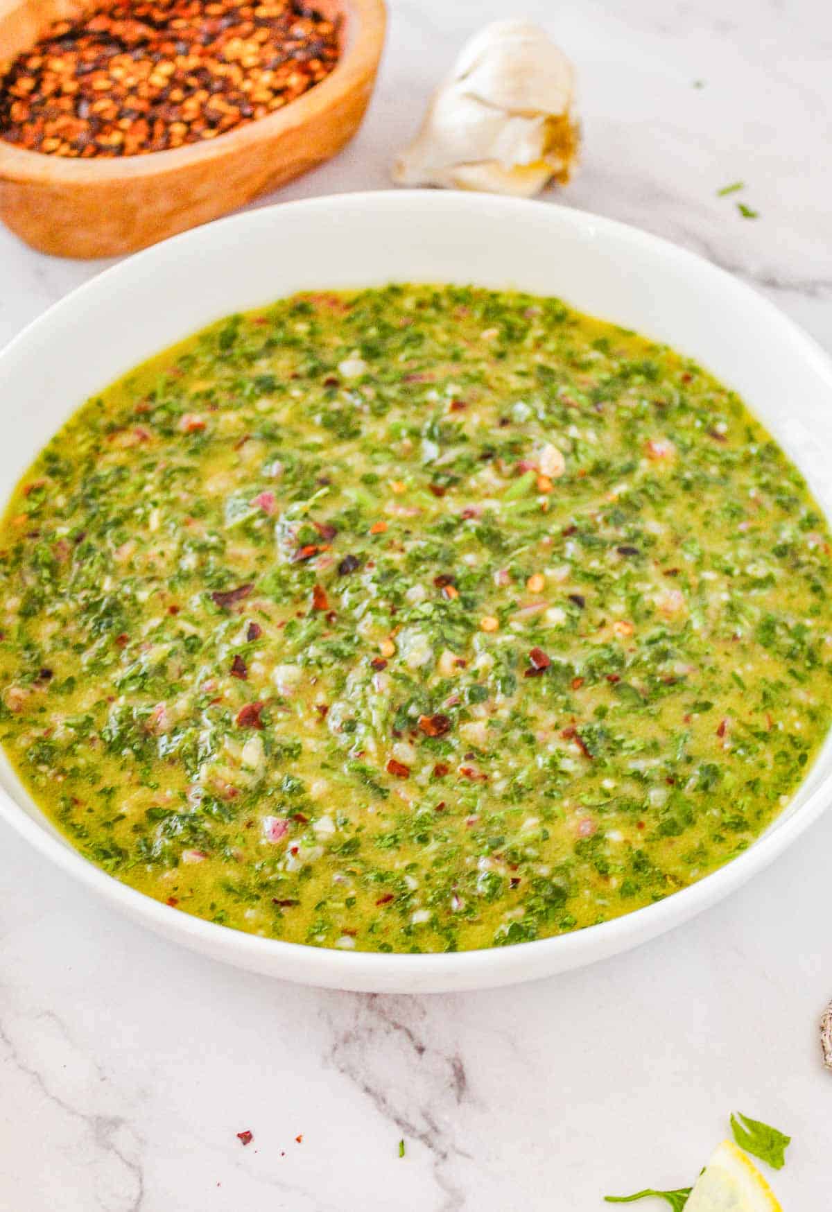 A piece of chicken breast on a white plate topped with Chimichurri sauce