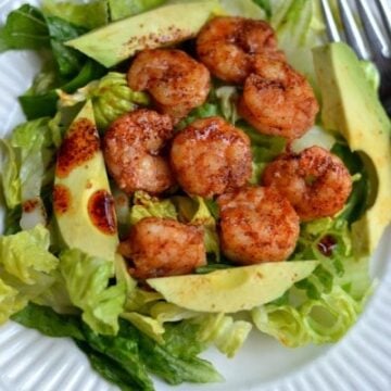 A plate with salad topped with spicy shrimp and avocado