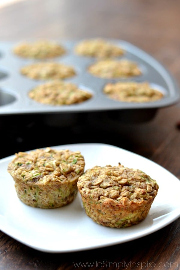 These Zucchini Banana Oatmeal Muffins are an incredible, healthy breakfast. Made with no refined sugar, oil or flour, they are wonderfully moist and perfect for on the go. Two Zucchini Banana Oatmeal Muffins on a white plate with muffin tin in the background