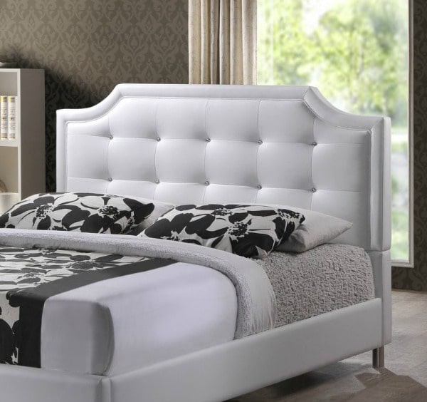 A bed with a white tuffed upholstered headboard and black floral pillows