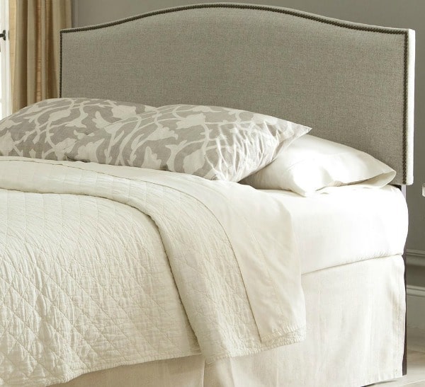 A bed with a tan upholstered headboard and cream bedding