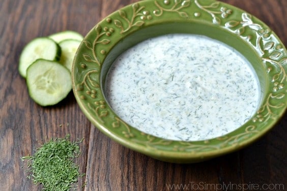 A close up of a A green bowl of Cucumber Dill sauce on a wood table