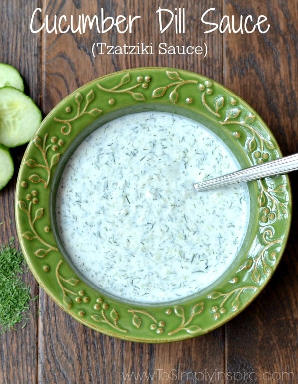 A green bowl of Cucumber Dill sauce with a spoon in it on a wood table 