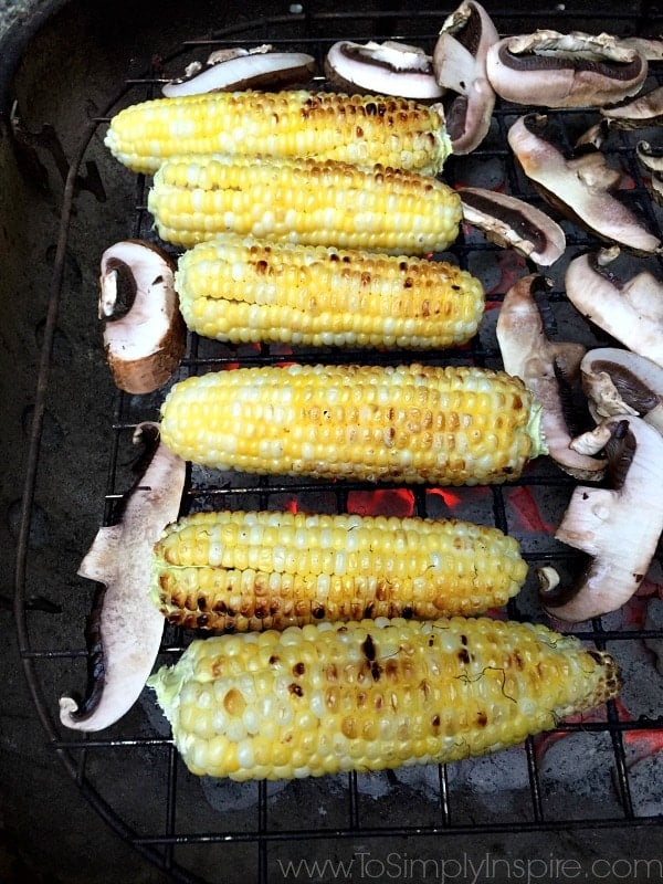 six ears of corn and portobello mushrooms cooking on a grill