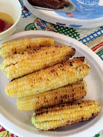 a white plate with grilled corn on the cob stacked on it