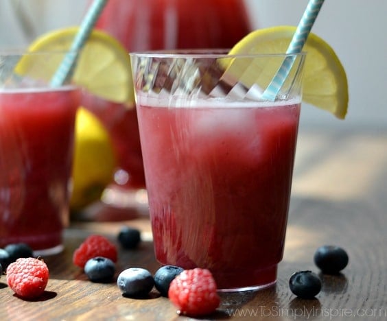 a cup of punch on a table with blueberries and raspberries 