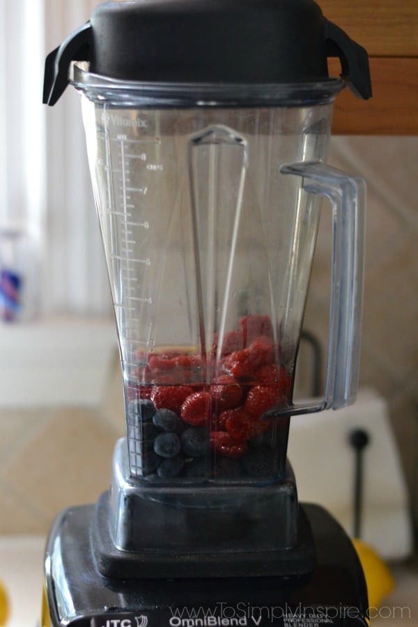 A blender sitting on a counter with blueberries and raspberries
