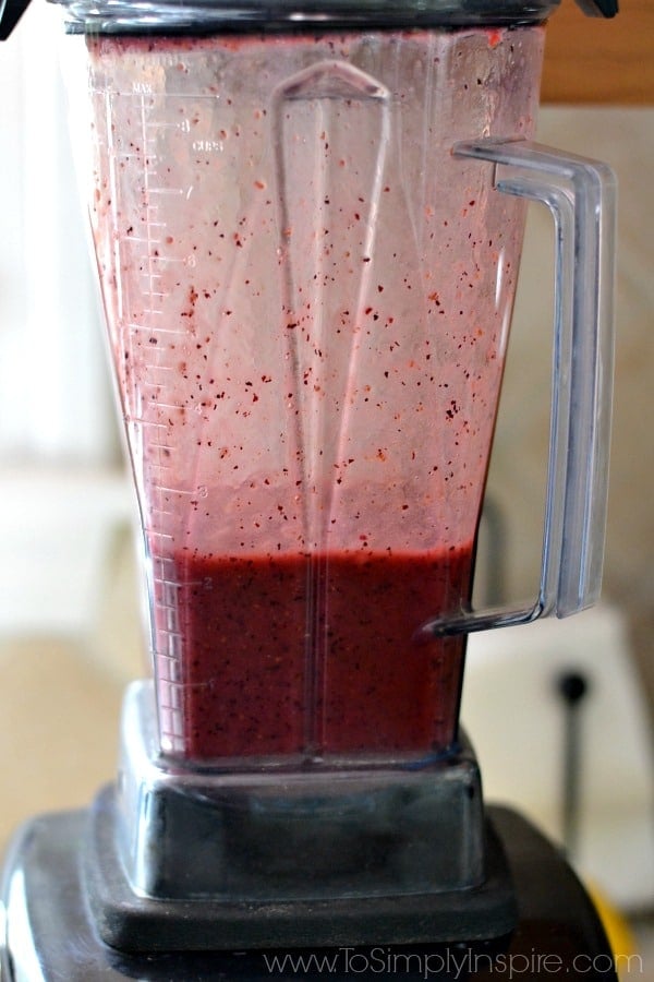 A close up of a blender mixing raspberries and blueberries