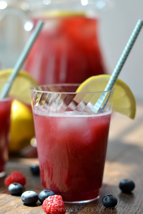 A close up of a red beverage in a cup on a table, with a lemon wedge and straw
