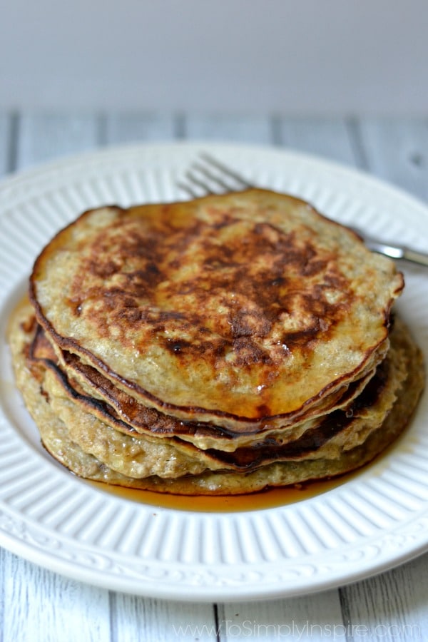 A stack of Banana Pancakes on a white plate covered in syrup