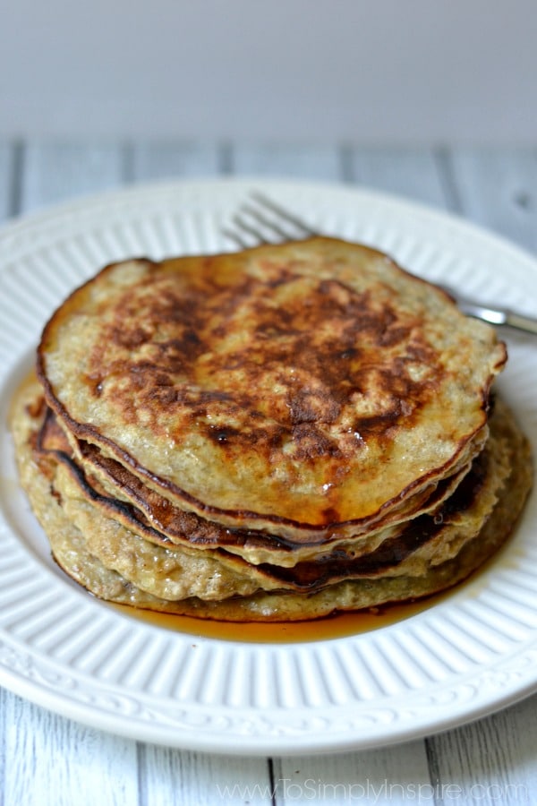 A stack of Banana Pancakes on a white plate covered in syrup