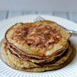 A stack of Banana Pancakes on a white plate covered in syrup