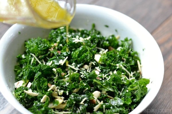 A bowl of kale salad, with dressing being poured over.