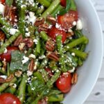 A bowl of salad with spinach asparagus and tomatoes with pecans and feta cheese