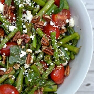 A bowl of salad with spinach asparagus and tomatoes with pecans and feta cheese