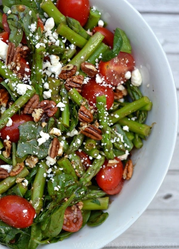a white bowl filled with a asparagus, spinach and tomato salad
