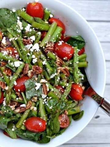 closeup of a salad with asparagus and tomatoes in the white bowl