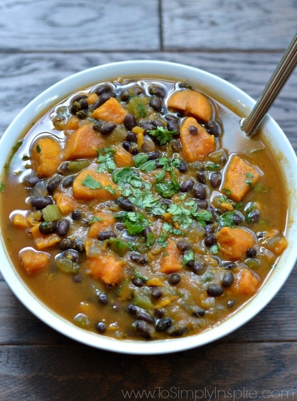 A white bowlful of sweet potato and black bean soup with a spoon