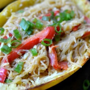 closeup of spaghetti squash with sliced red peppers and sliced scallions.