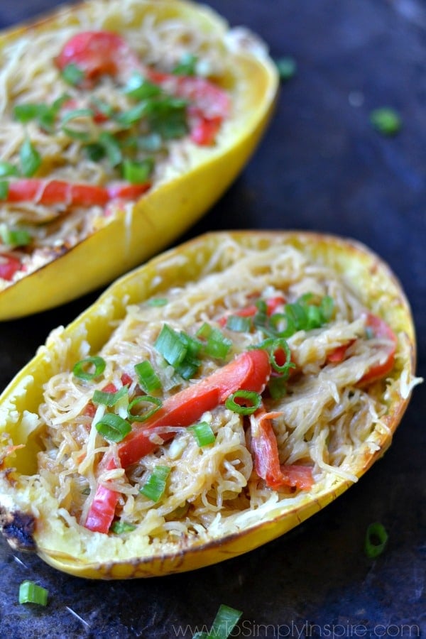 A close up of a two spaghetti squash halves with red pepper slices and green onions